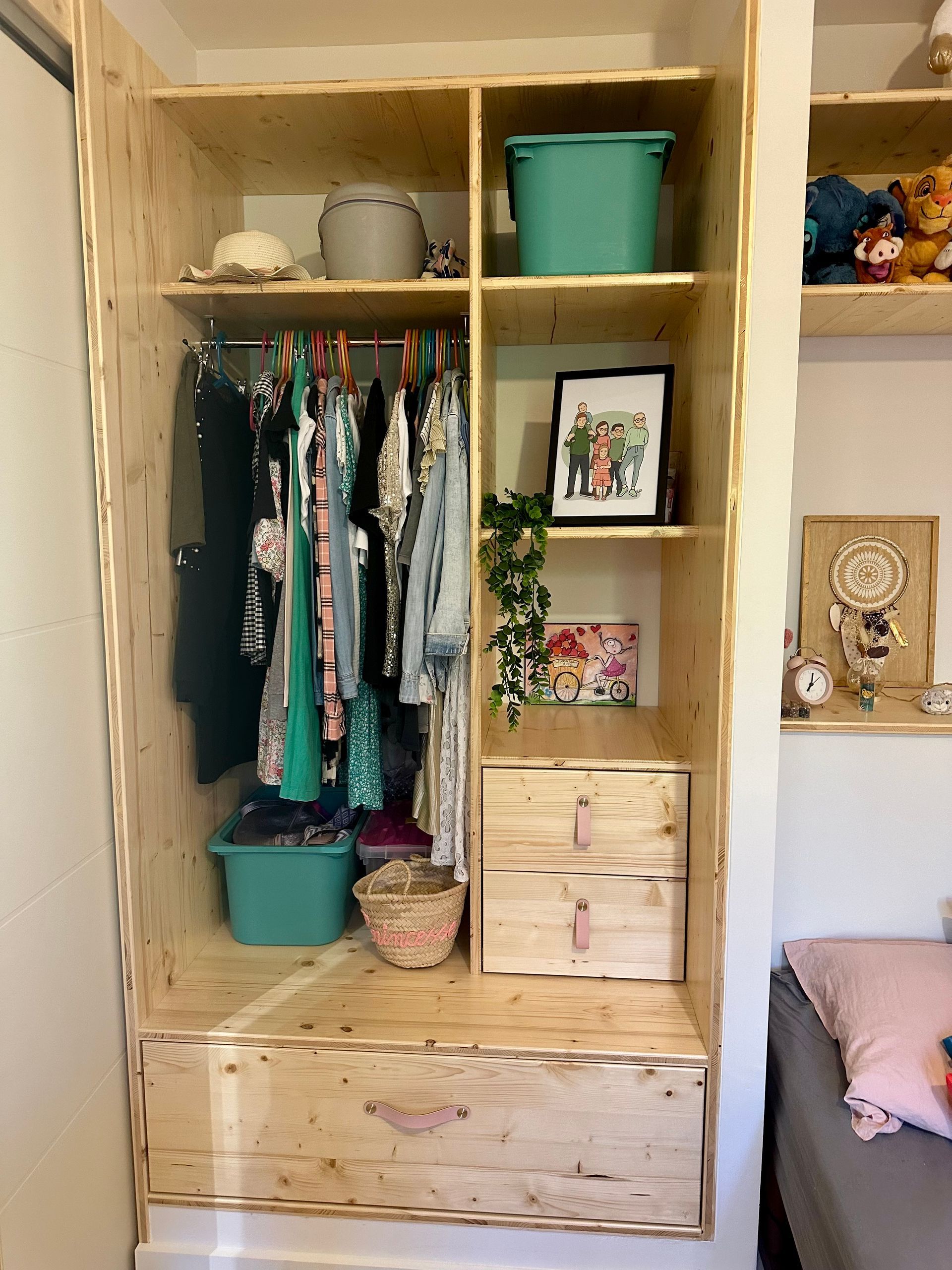 Armoire ouverte avec vêtements suspendus, tiroirs, paniers et étagères dans une chambre confortable.