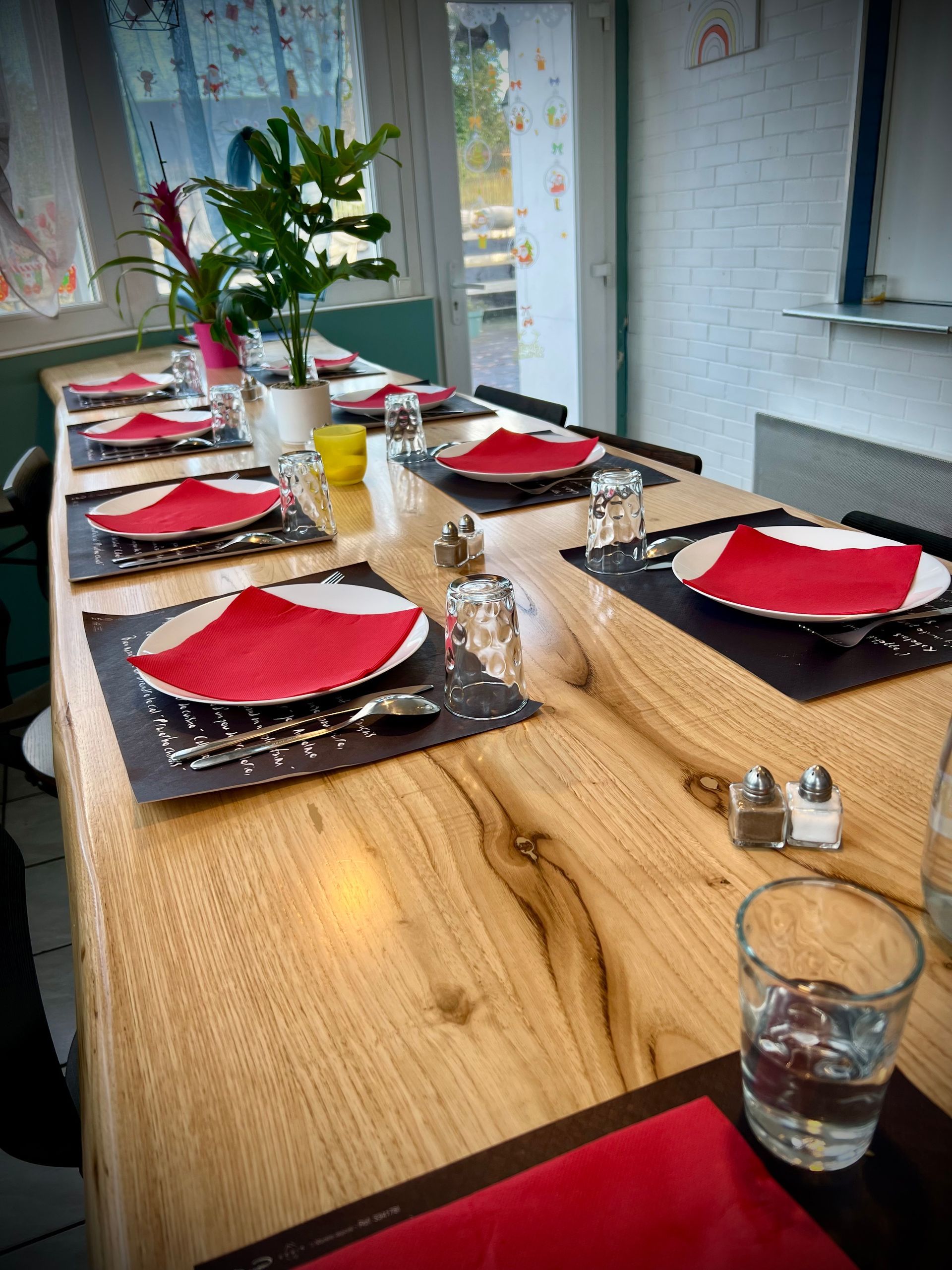 Une table à manger avec des serviettes rouges, des verres et des assiettes sur une table en bois dans une pièce lumineuse.