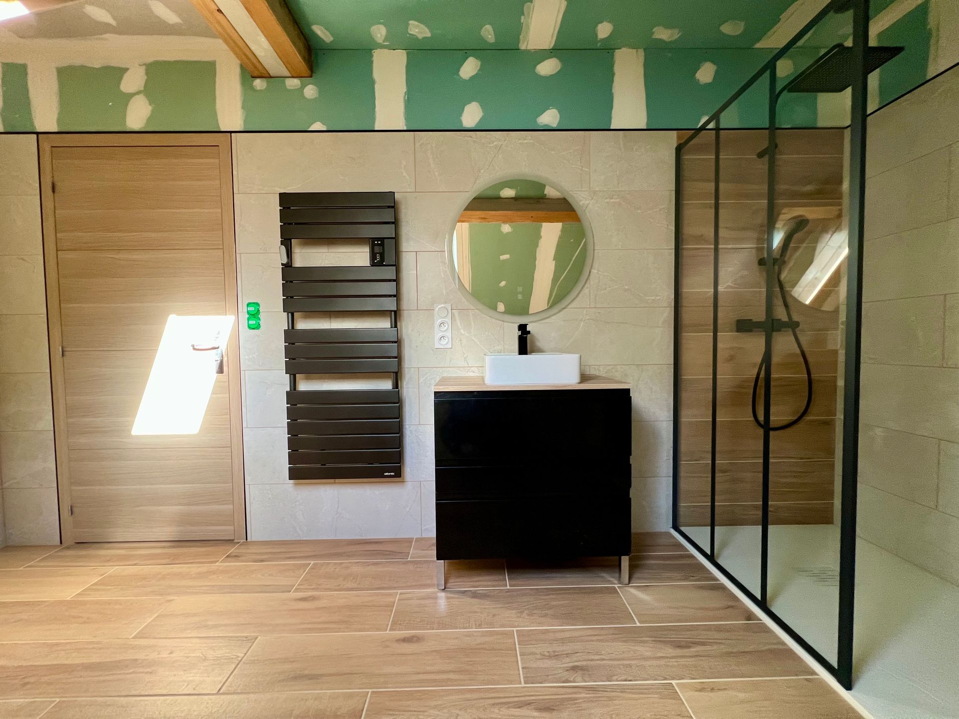 Salle de bains moderne avec portes en bois, meuble-lavabo, miroir rond et cabine de douche en verre.