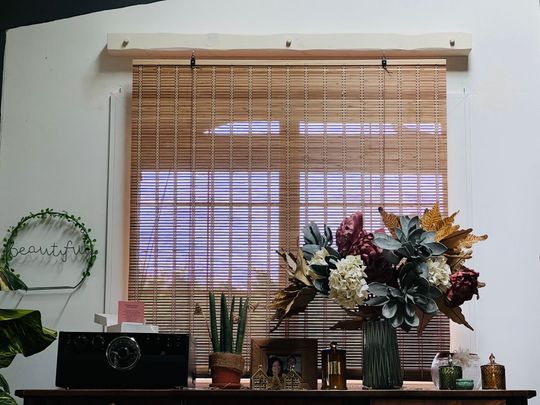 Un rebord de fenêtre décoré de stores en bambou, de plantes en pot et d'une composition florale dans une pièce confortable.