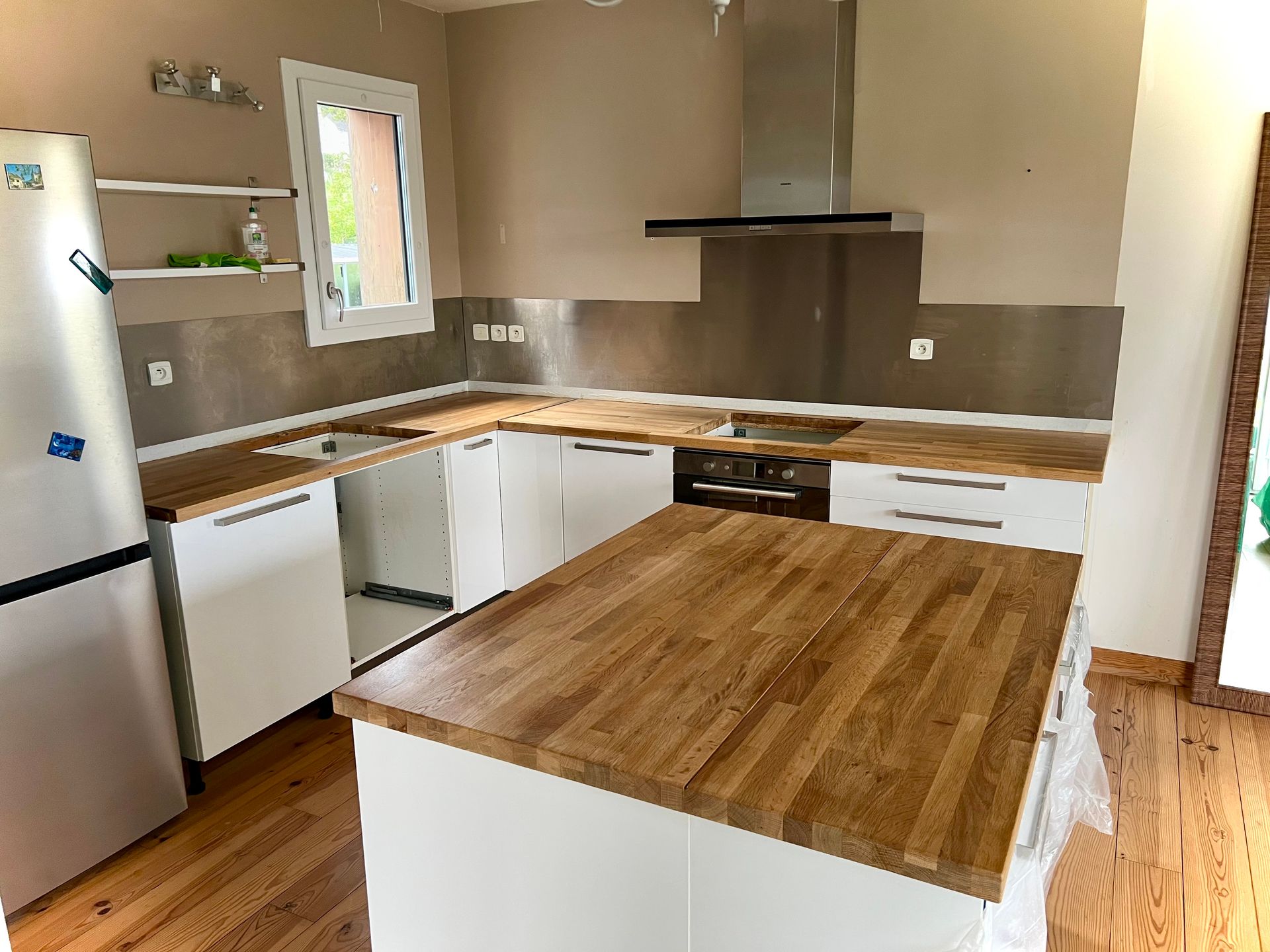 Cuisine moderne avec armoires blanches, comptoirs en bois, hotte en acier inoxydable et îlot central.