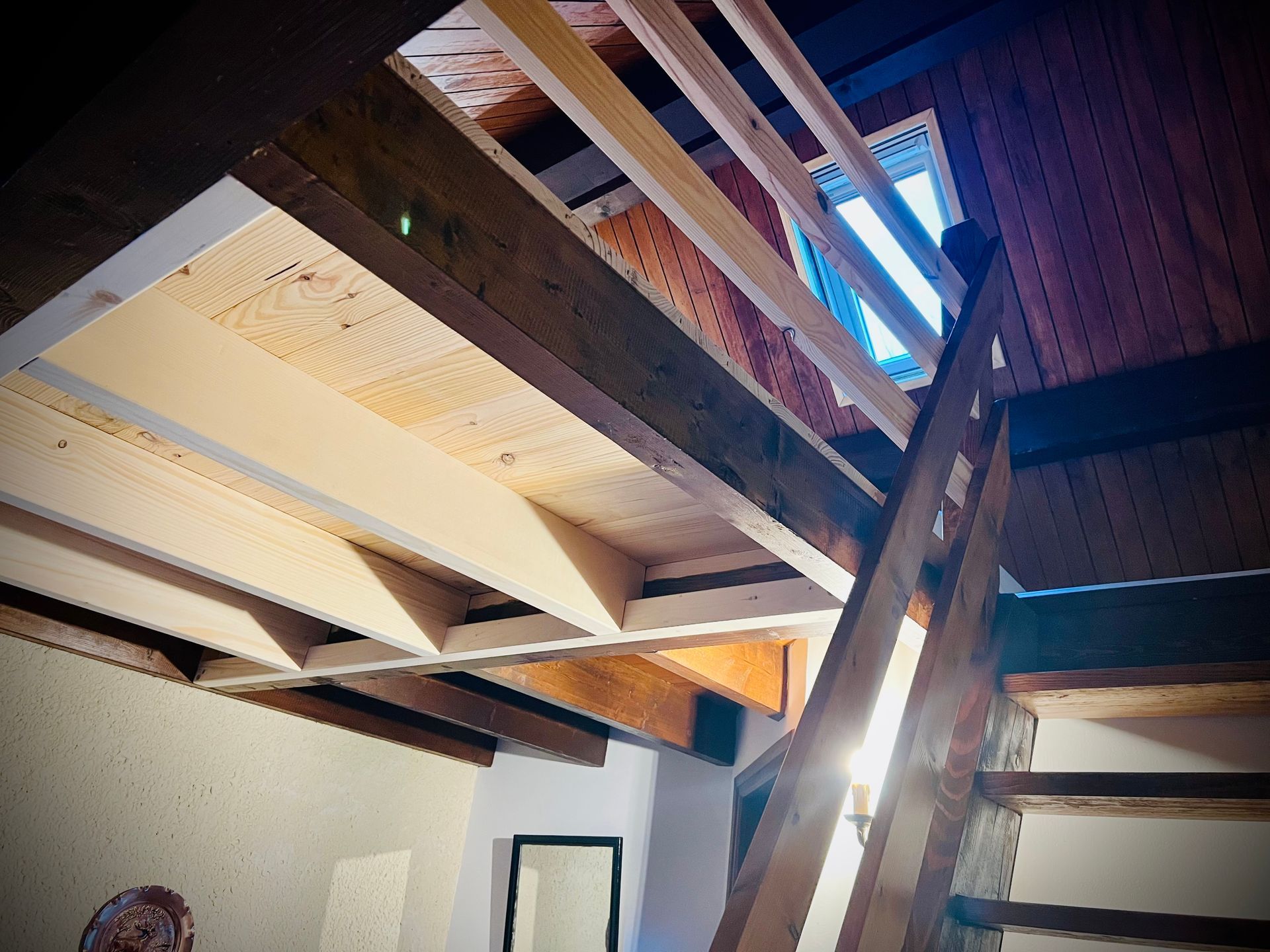 Plafond intérieur avec poutres en bois apparentes et puits de lumière, vu d'en bas.
