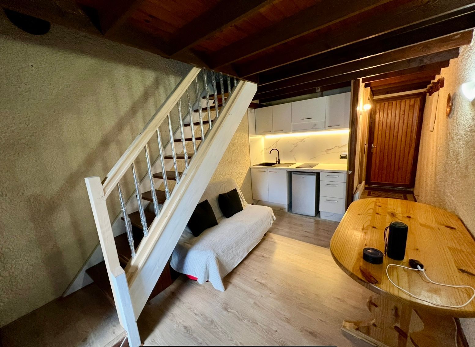 Loft confortable avec escalier, canapé, kitchenette et table à manger en bois sous un plafond bas.