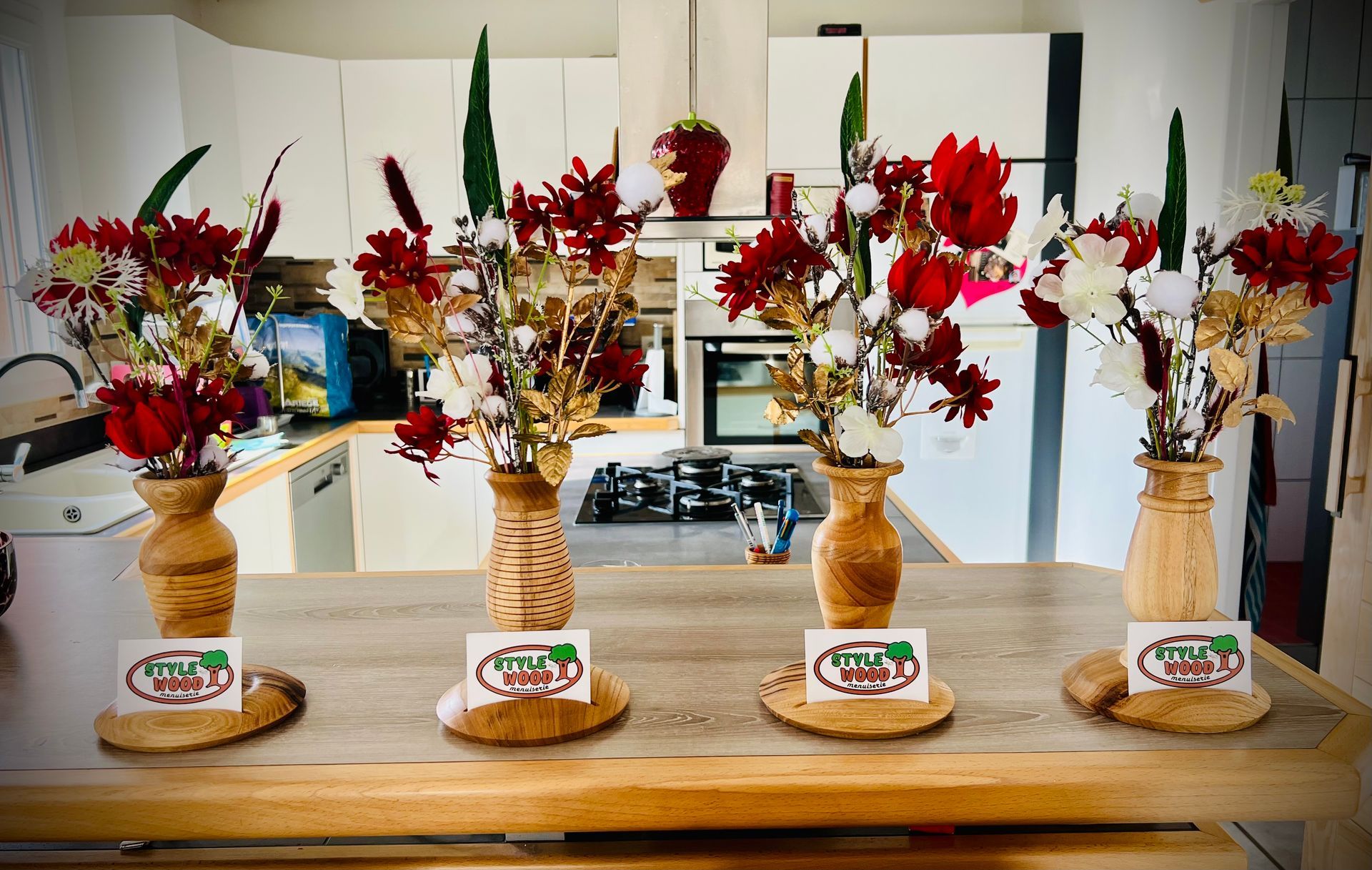 Quatre compositions florales avec des fleurs rouges et blanches sur une table en bois.