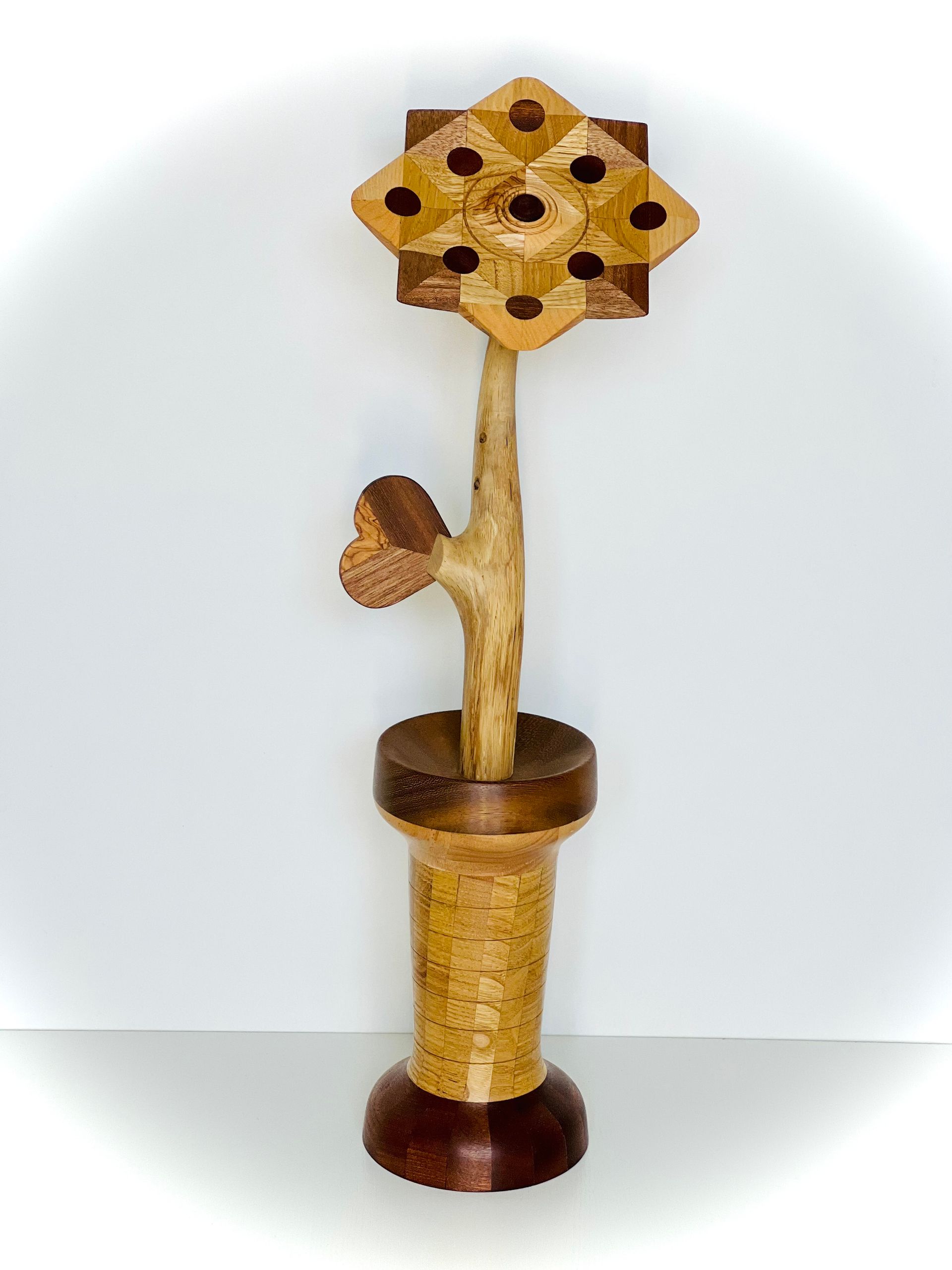 Petite sculpture décorative en bois représentant une maison d'oiseaux, posée sur un support, avec un sommet hexagonal jaune et une base brun foncé.