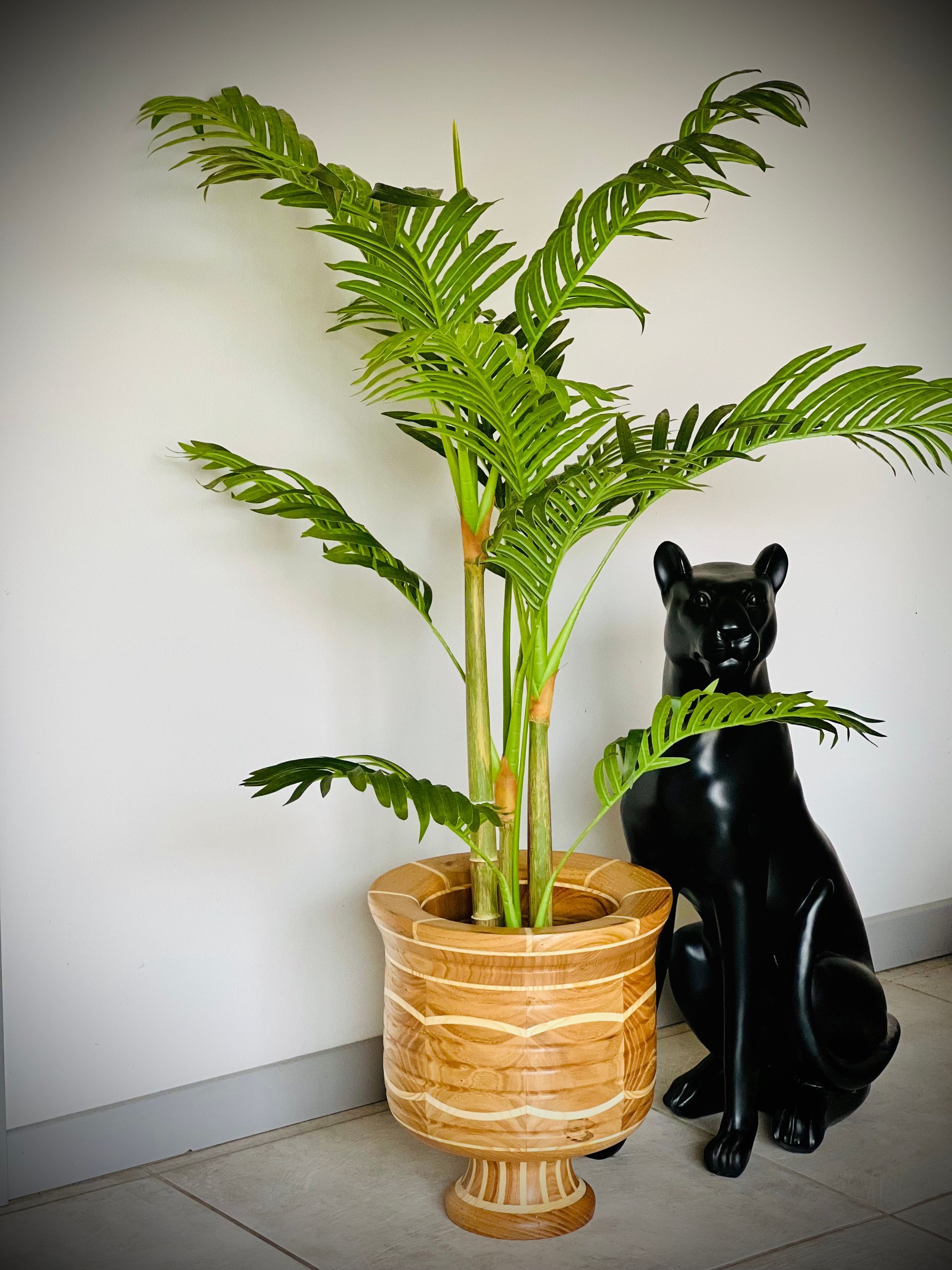 Une fougère en pot à côté d'une statue de chat noir dans un coin sur un sol gris.