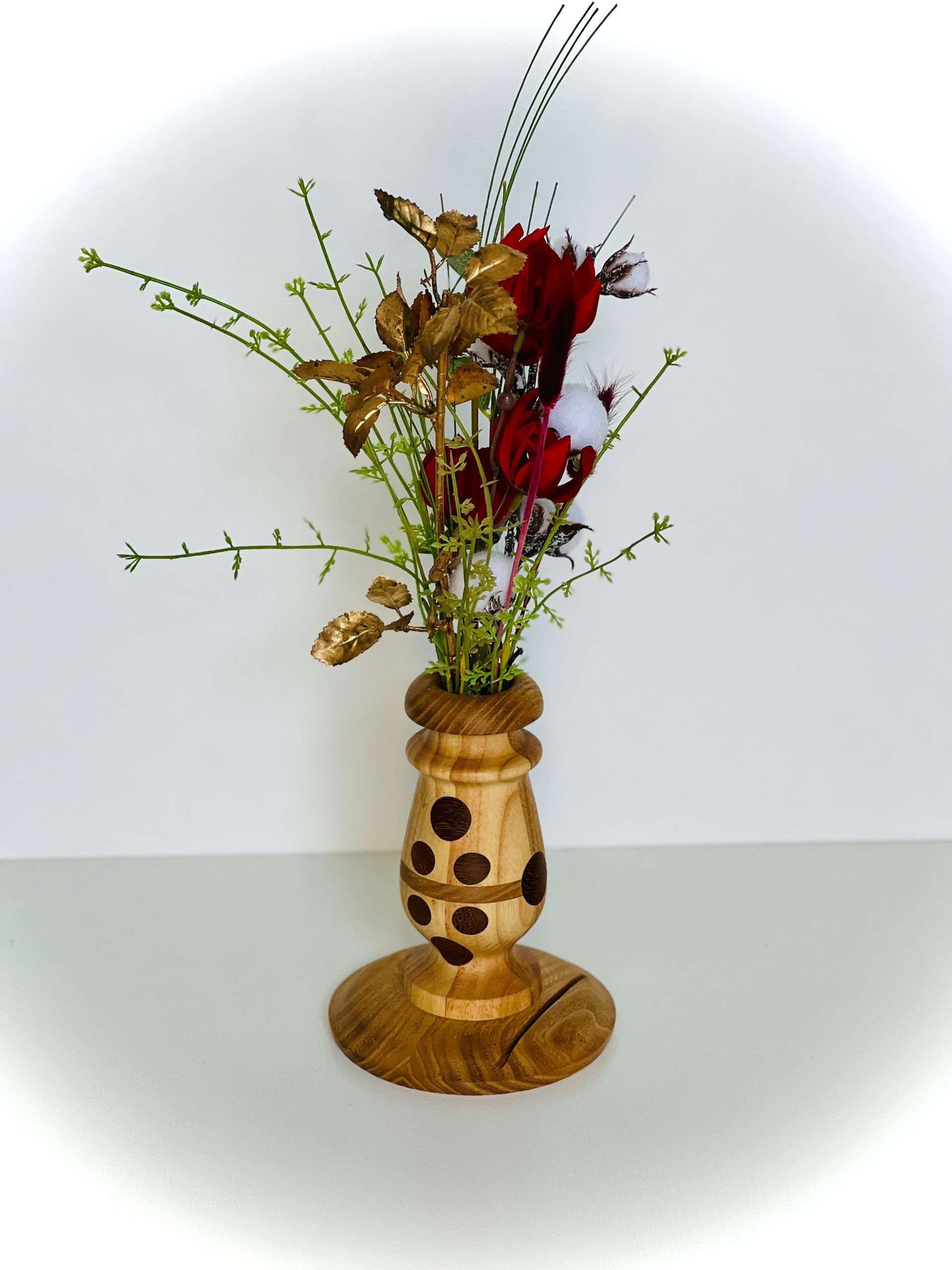 Grande composition florale avec des tiges rouges, jaunes et vertes dans un vase en bois tacheté sur un socle rond