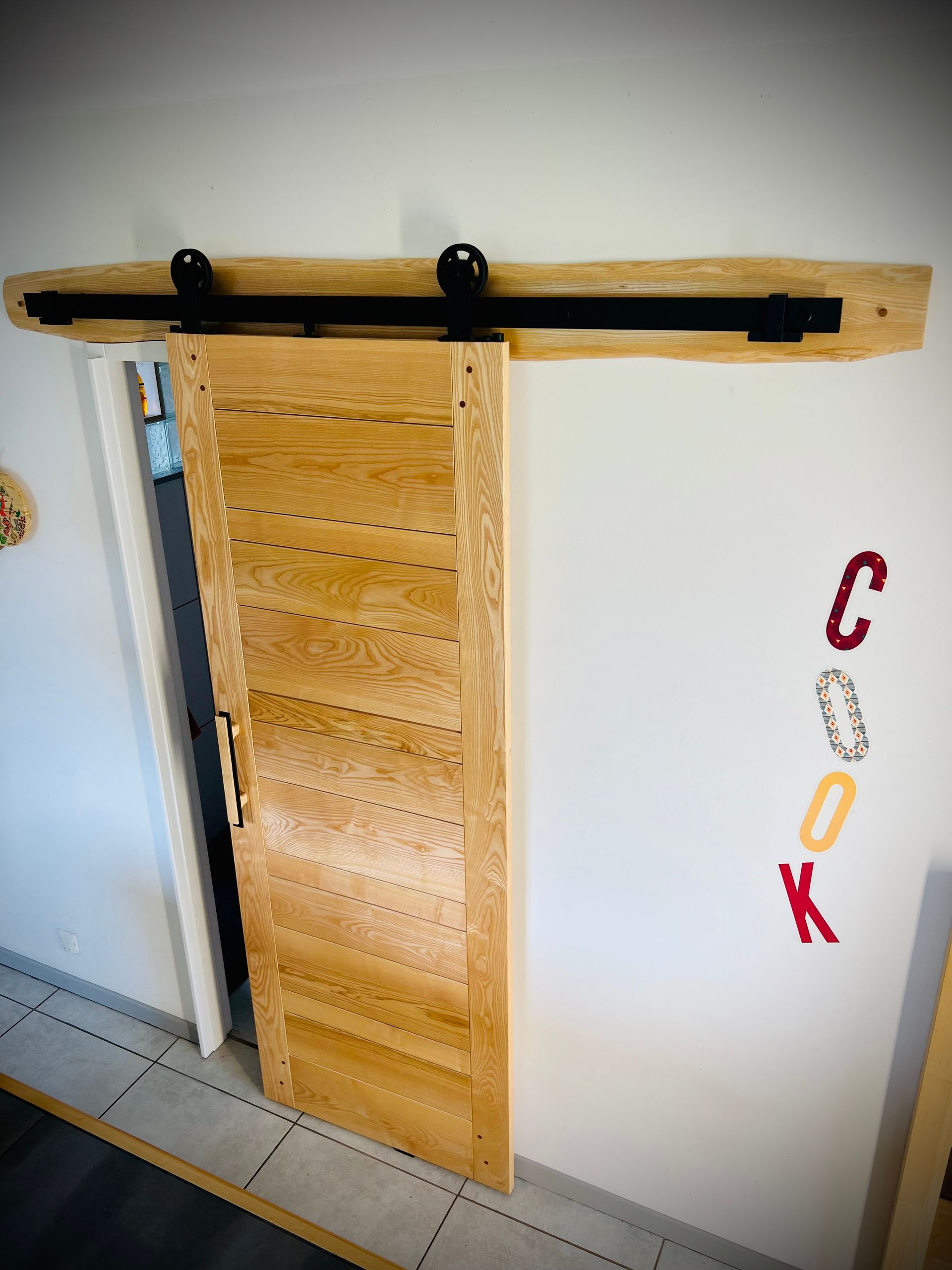Porte coulissante en bois avec quincaillerie noire sur un mur blanc.