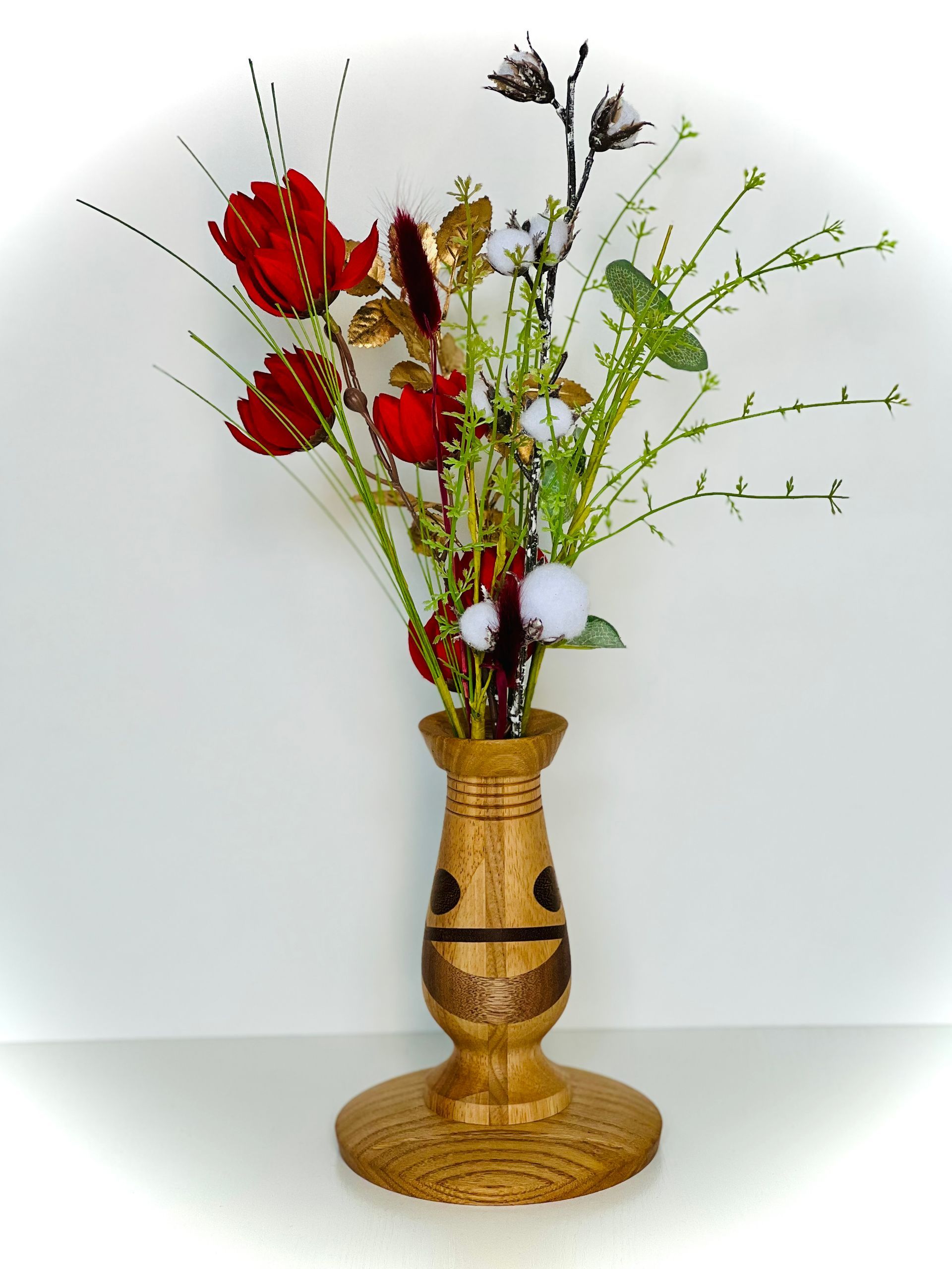 Vase en bois avec des fleurs séchées rouges et vertes sur fond blanc