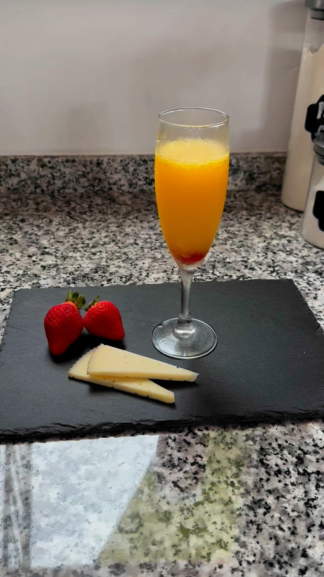 Un vaso de jugo de naranja está sobre una tabla de cortar al lado de fresas y queso.
