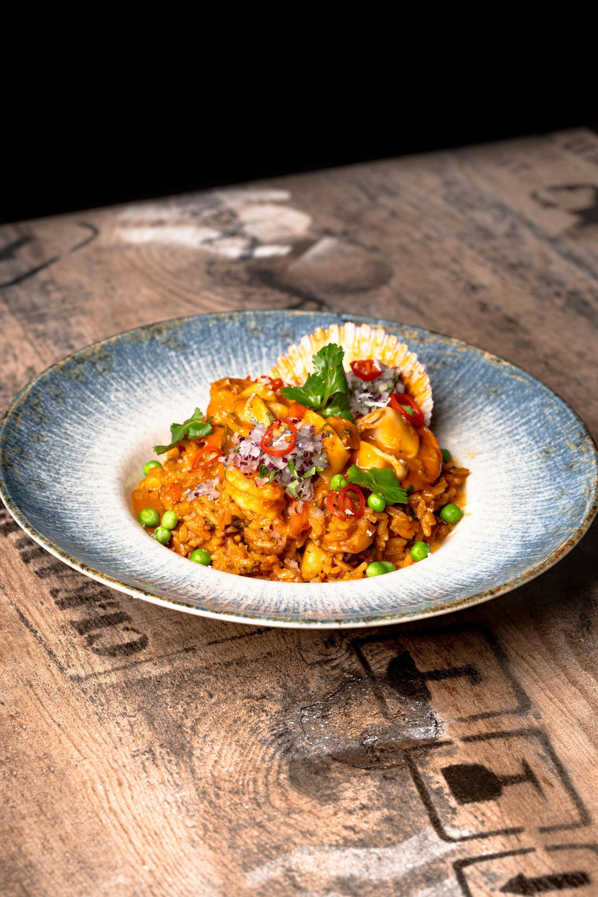 Una sartén con guisado de pollo con zanahorias y perejil sobre una tabla de cortar.