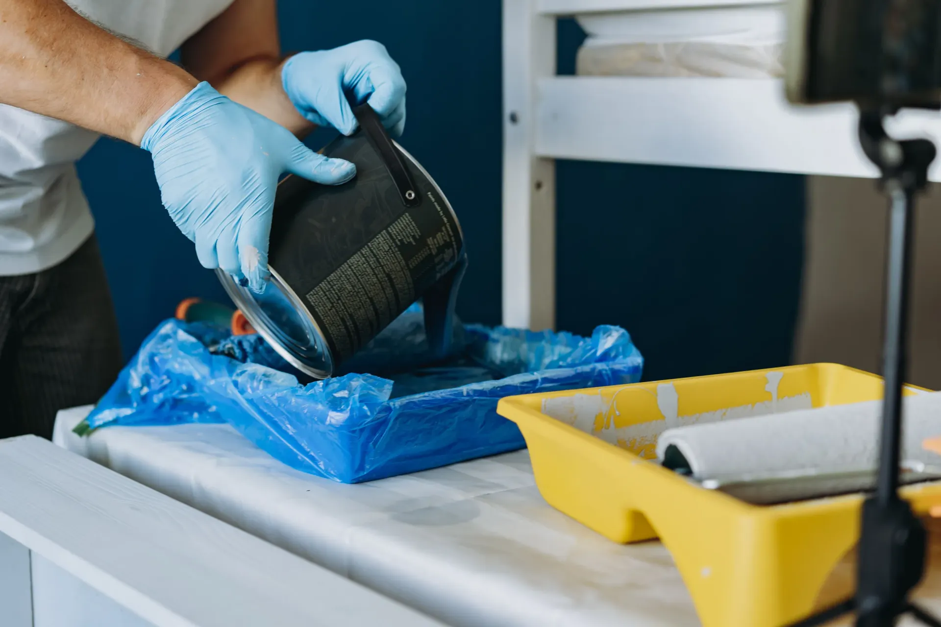 Persona vertiendo pintura azul de una lata en una bandeja.