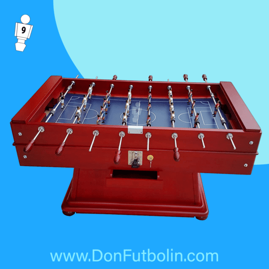 Mesa de futbolín roja con superficie de juego azul y figuras de jugadores; sobre un fondo azul.