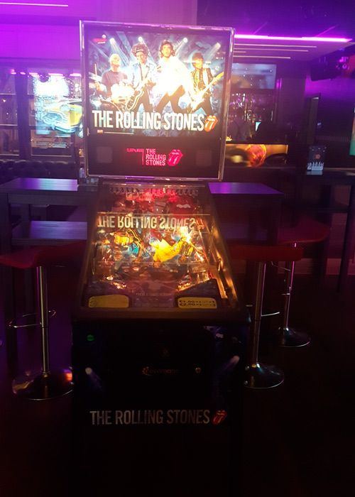 Una máquina de pinball de los Rolling Stones en una habitación con poca luz, con la banda en el cristal trasero. Detalles en rojo.