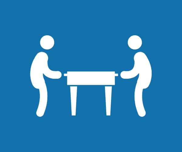 Dos personas levantando una mesa juntas sobre un fondo azul.