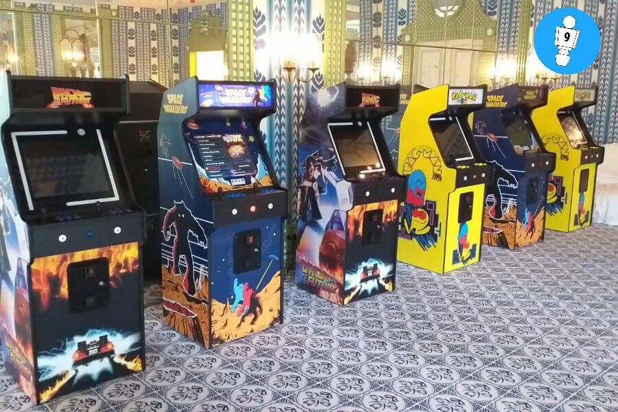 Una fila de máquinas de juegos arcade retro con gráficos coloridos, en el interior sobre una alfombra estampada.