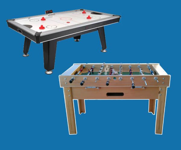 Una mesa de hockey de aire y un futbolín sobre un fondo azul. La mesa de hockey de aire es negra con discos rojos. El futbolín es de madera clara.