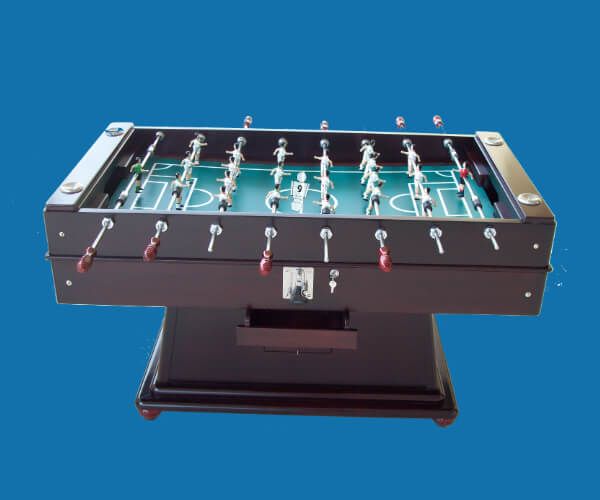 Mesa de futbolín sobre soporte de madera oscura, con campo de juego verde y jugadores sujetos a varillas.