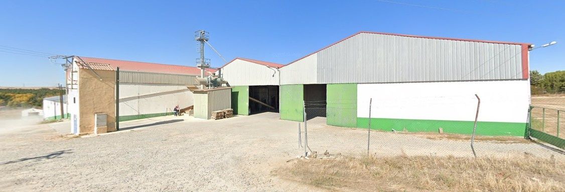 Casa de campo rural con edificios blancos y verdes bajo un cielo azul claro en un terreno de tierra.