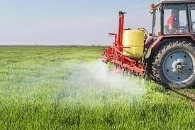 Tractor rociando fertilizante para cultivos en un campo verde.