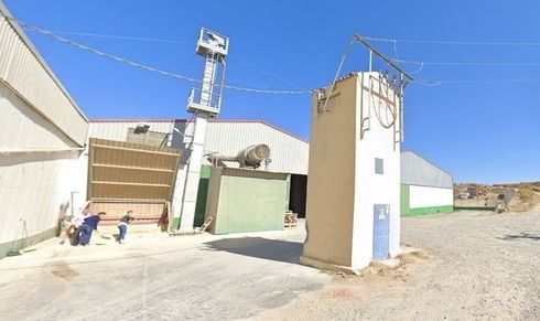 Entrada industrial con edificios blancos, un poste de servicios públicos y una persona cerca del lado izquierdo.