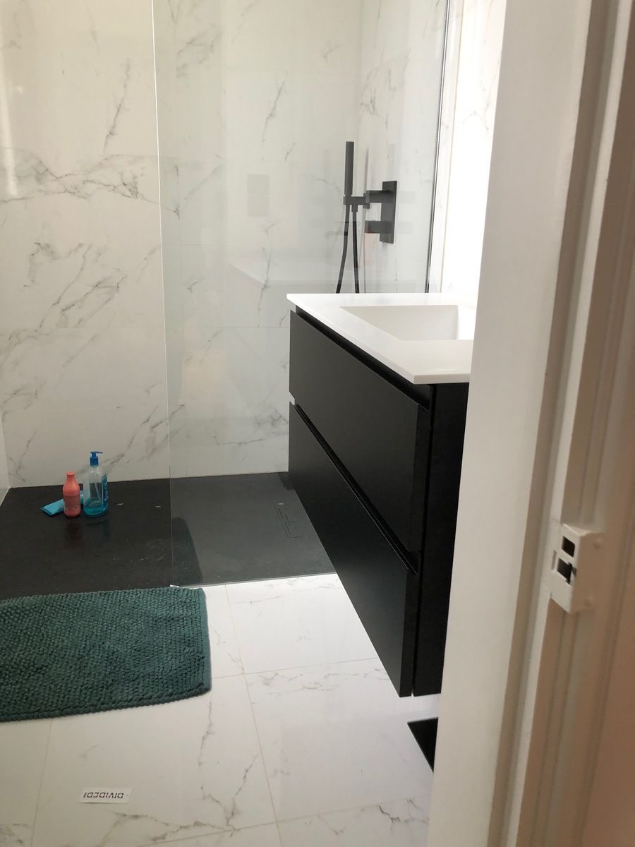 Salle de bains moderne avec meuble-lavabo noir, carrelage en marbre blanc, douche et tapis turquoise.