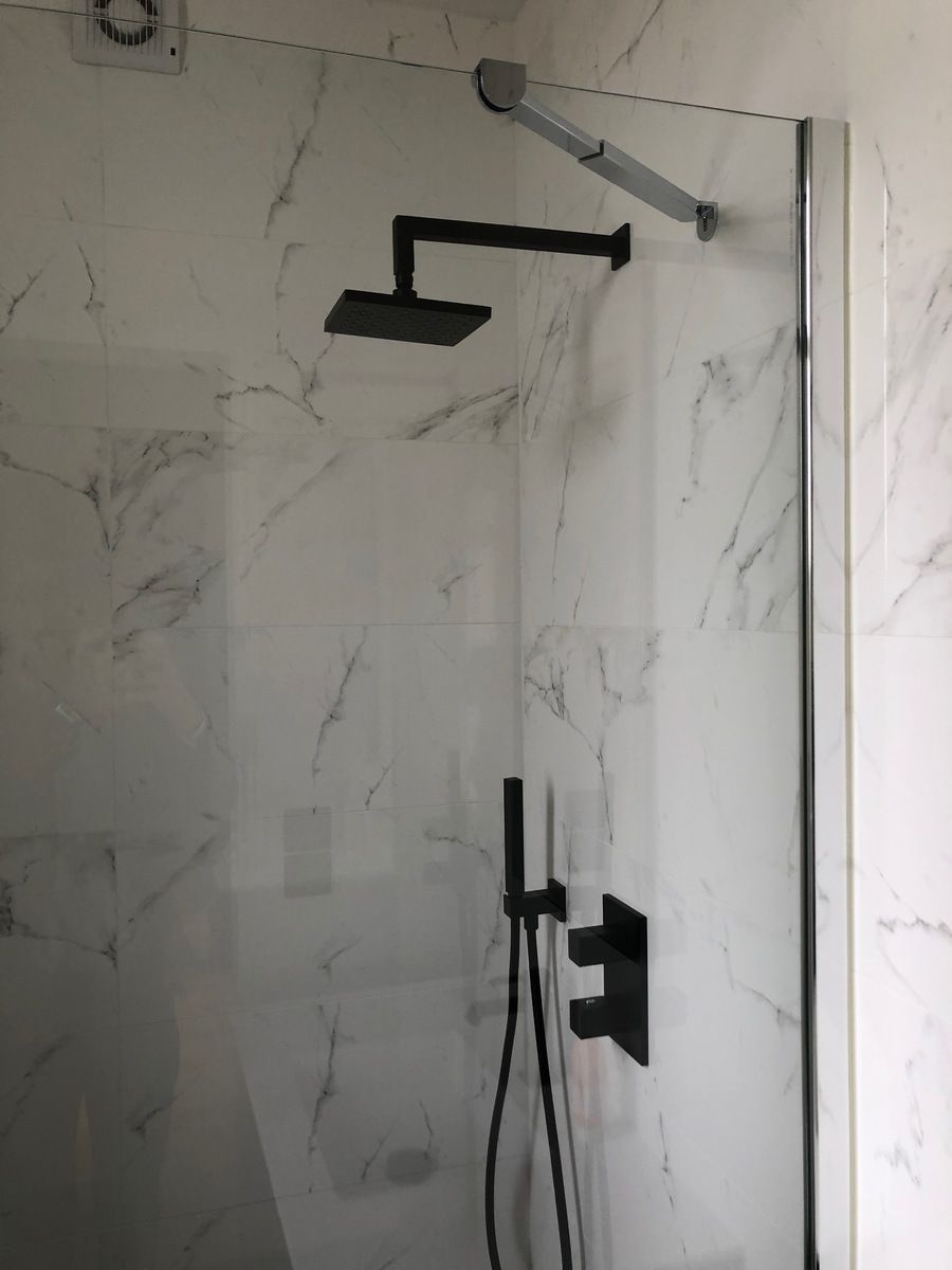 Pommeau de douche, robinet et douchette noirs dans une douche carrelée en marbre avec une porte en verre.