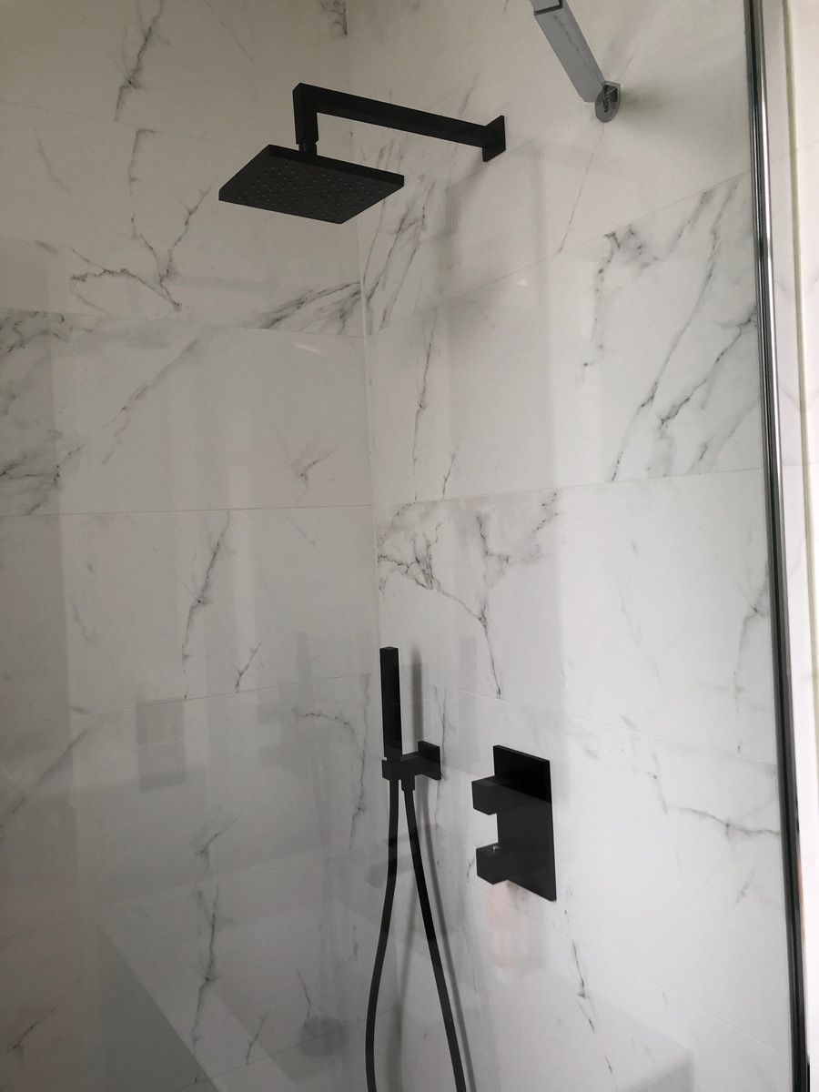 Robinetterie de douche noire contrastant avec le carrelage en marbre blanc dans une salle de bains.