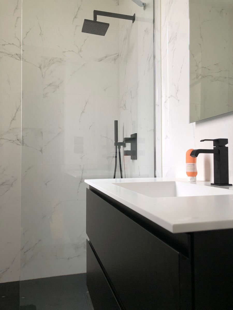 Salle de bains moderne avec meuble-lavabo noir, lavabo blanc, douche carrelée en marbre et robinetterie noire.