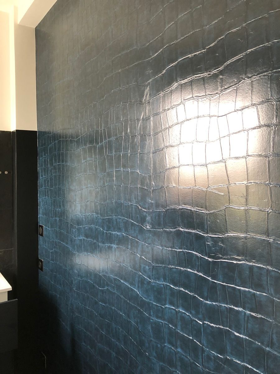 Mur bleu foncé à la texture de peau de crocodile, éclairé par un carré de lumière vive.
