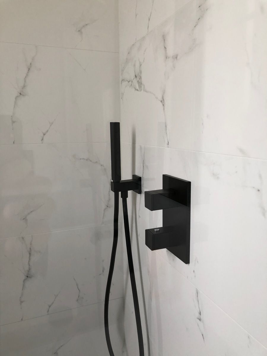 Robinetterie de douche noire sur un mur carrelé de marbre blanc.