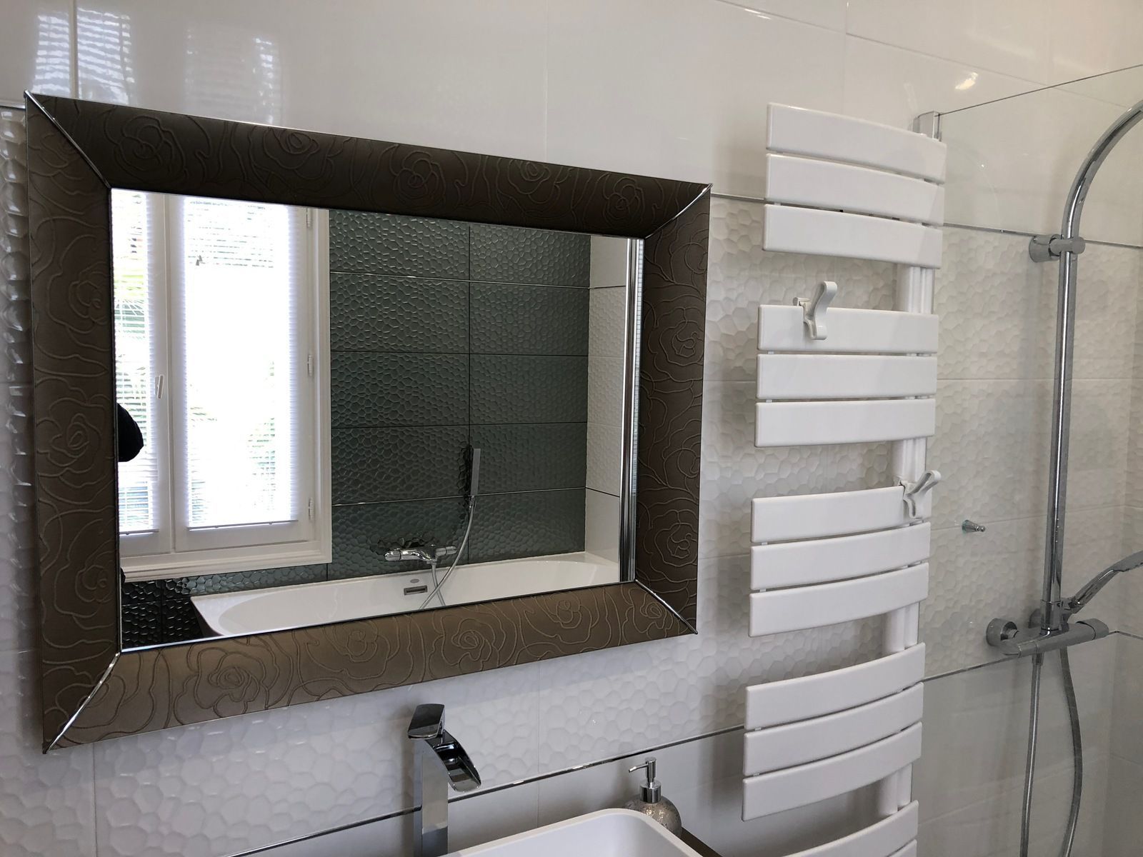 Salle de bains avec un grand miroir encadré, un porte-serviettes et une douche.