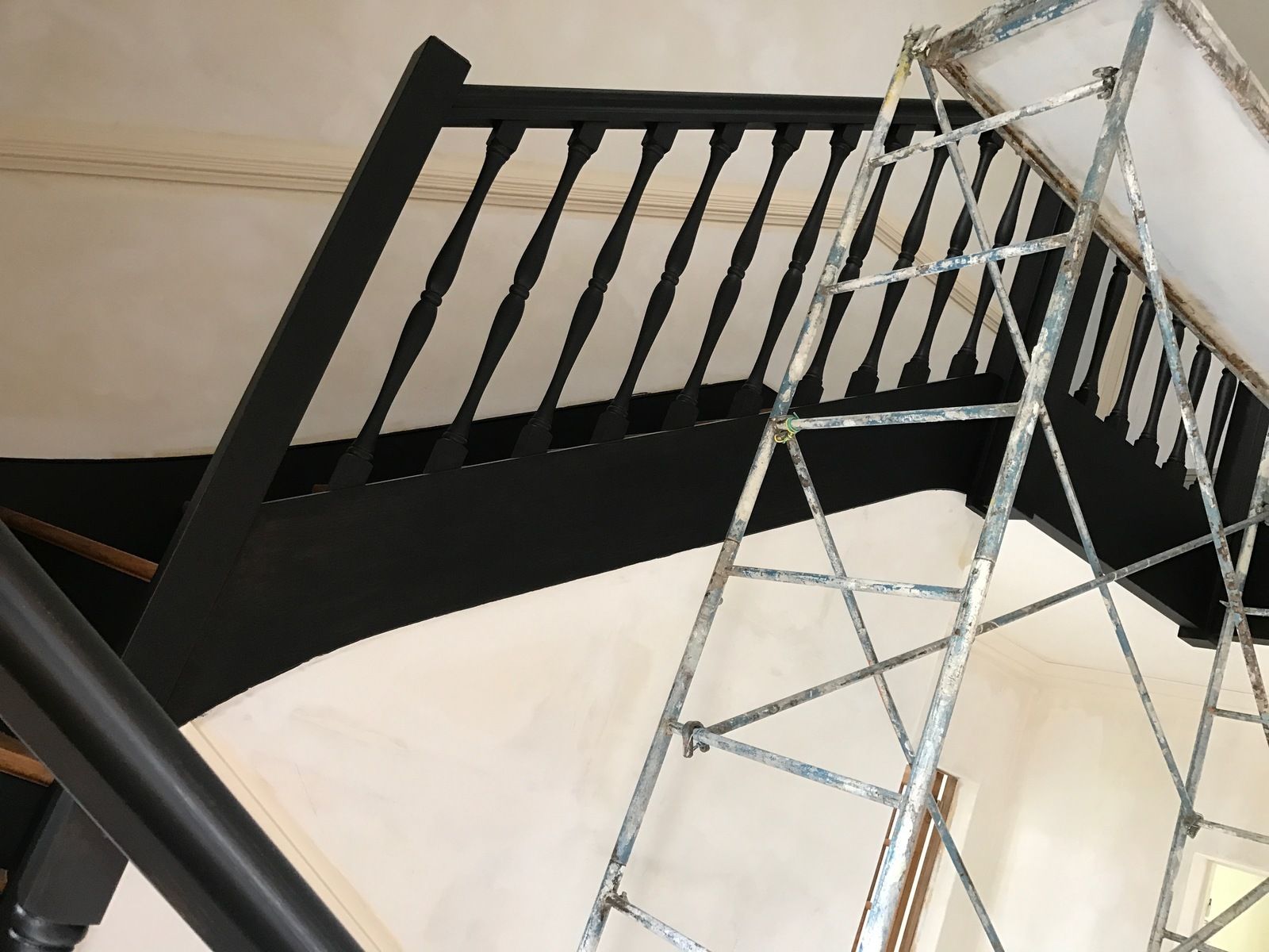 Escalier noir devant un mur blanc. Une échelle métallique est appuyée contre le mur.