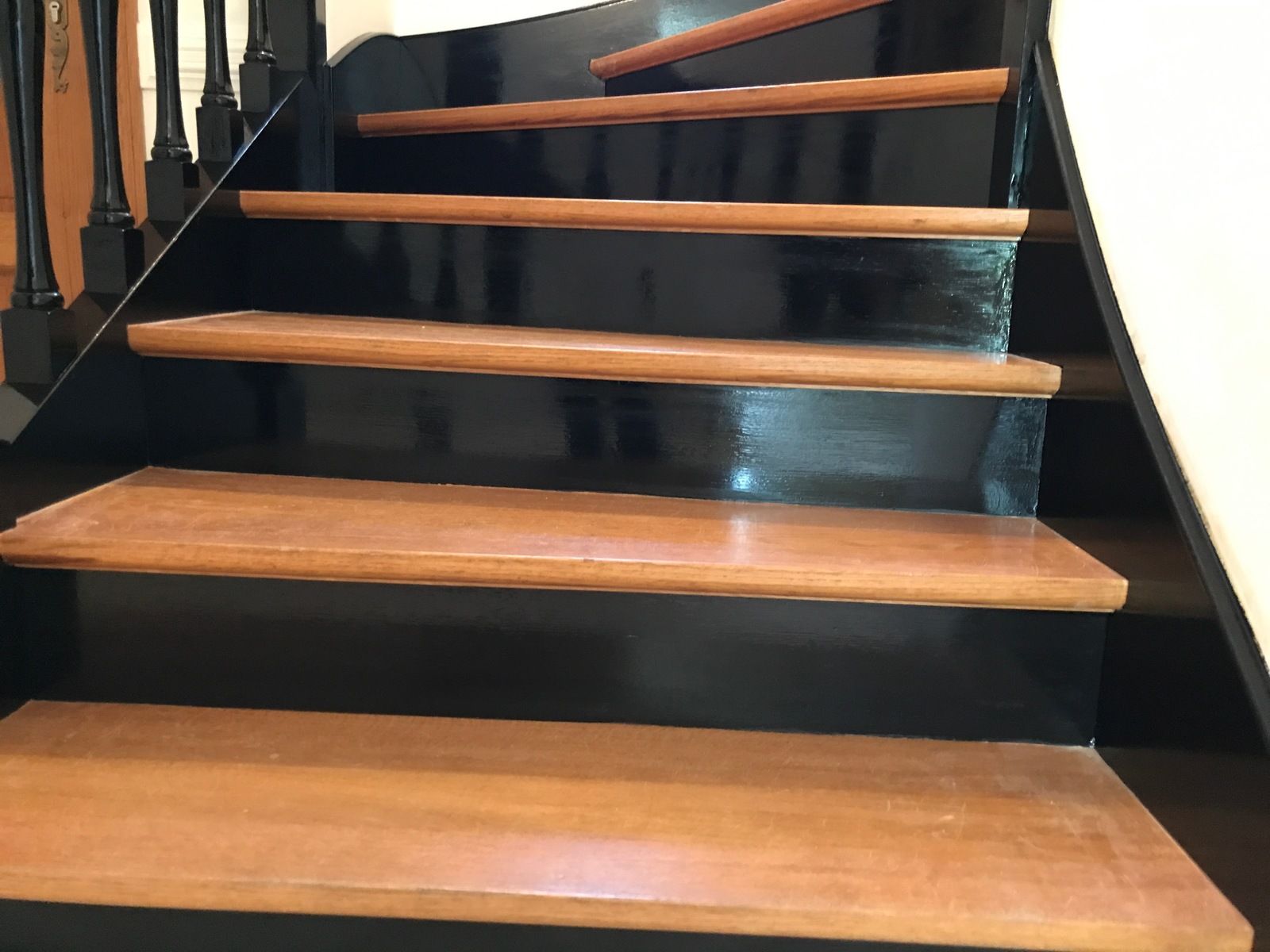 Escalier en bois avec marches marron et contremarches noires, éclairé par le haut.