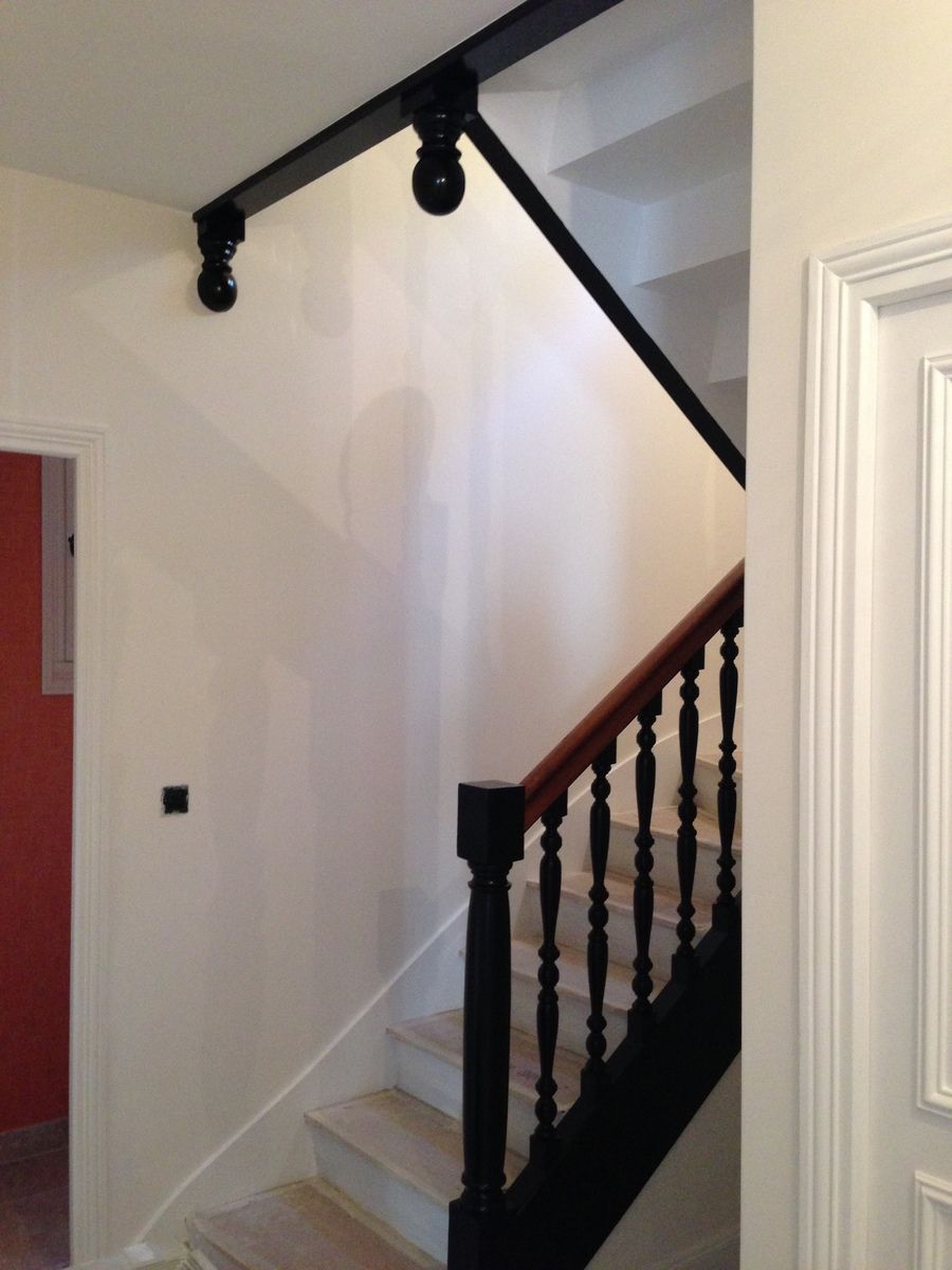 Escalier avec rampe et main courante noires, murs couleur crème, éclairage sur rail.