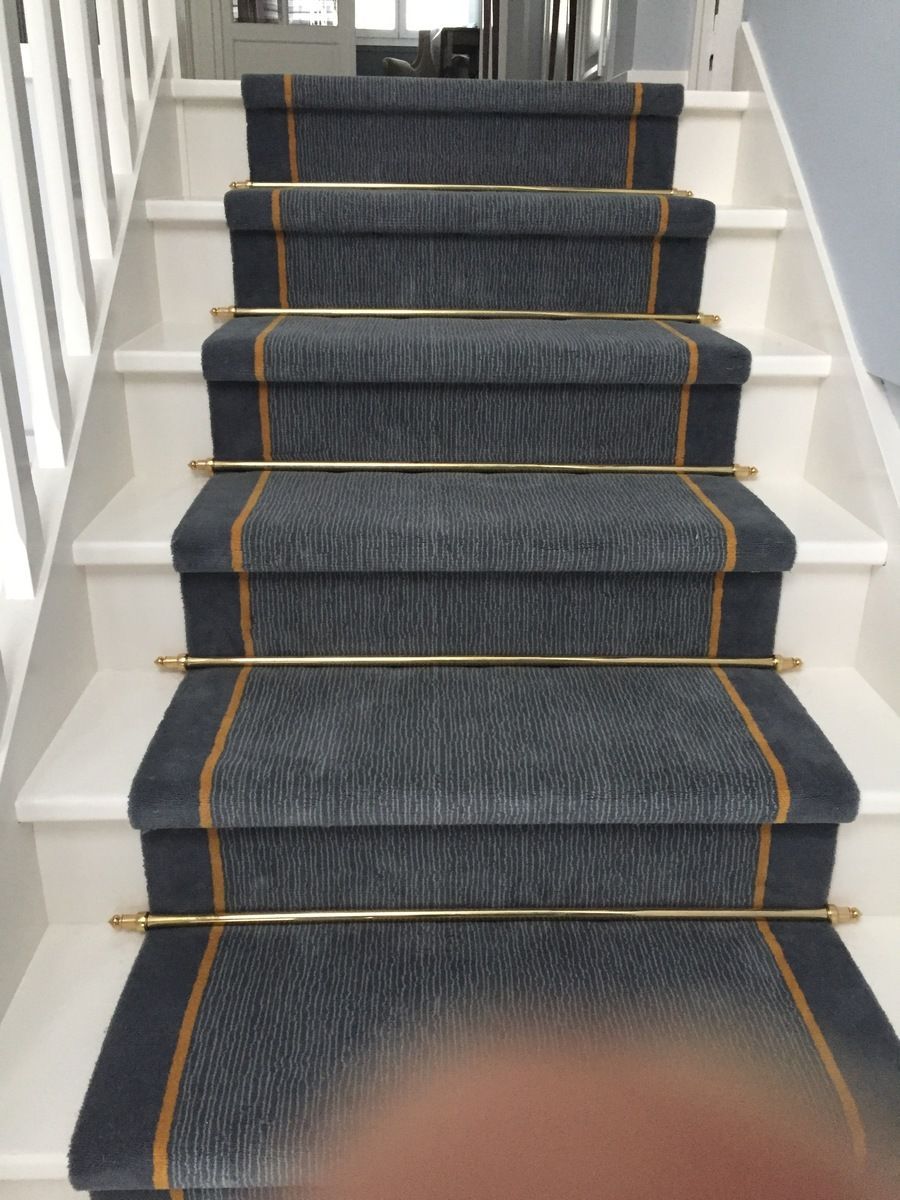 Escalier avec tapis gris et barres en laiton, contremarches et rampe blanches.