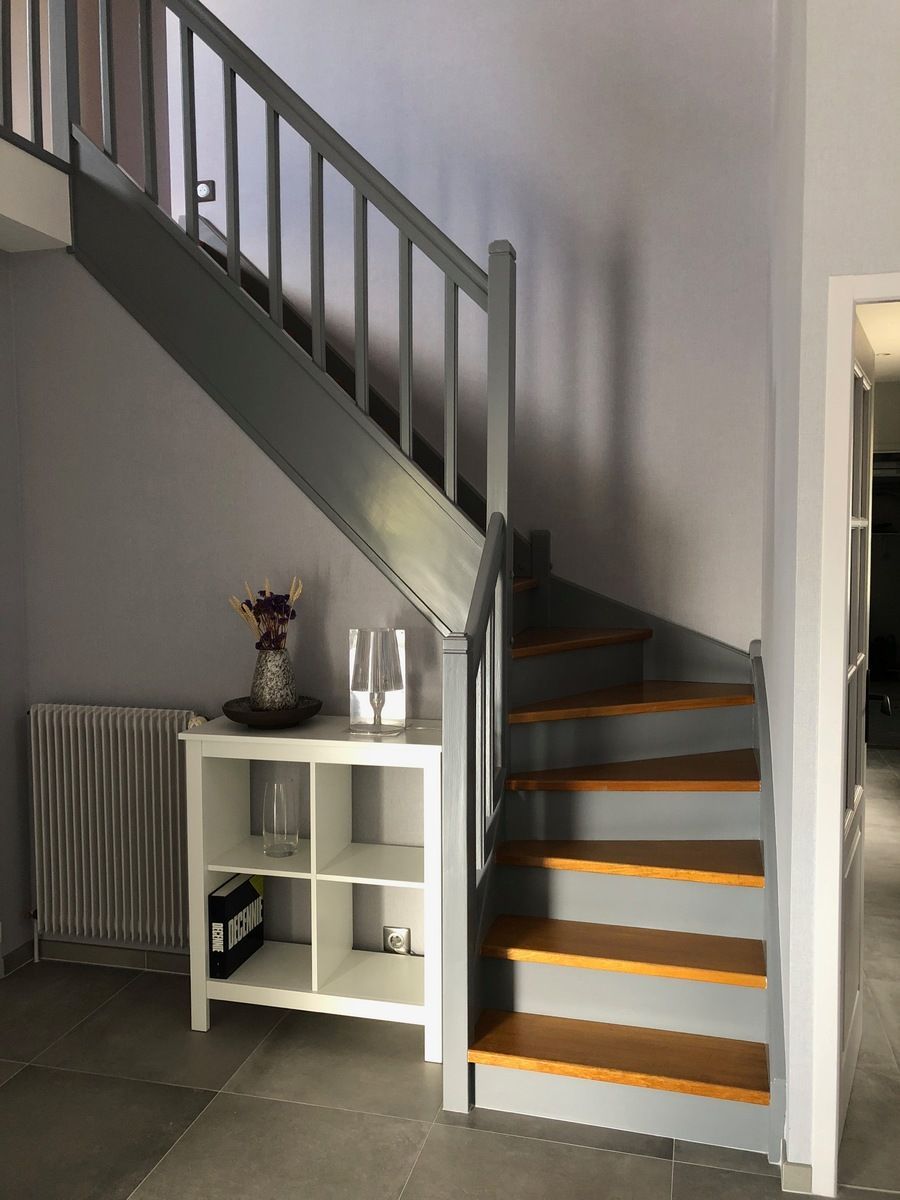 Escalier avec marches en bois et rampe grise, à côté d'une étagère blanche et d'un radiateur.