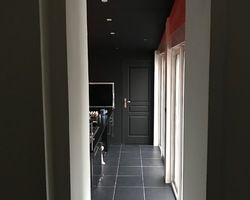 Couloir sombre avec porte noire, sol carrelé et supports verticaux blancs. Télévision visible.