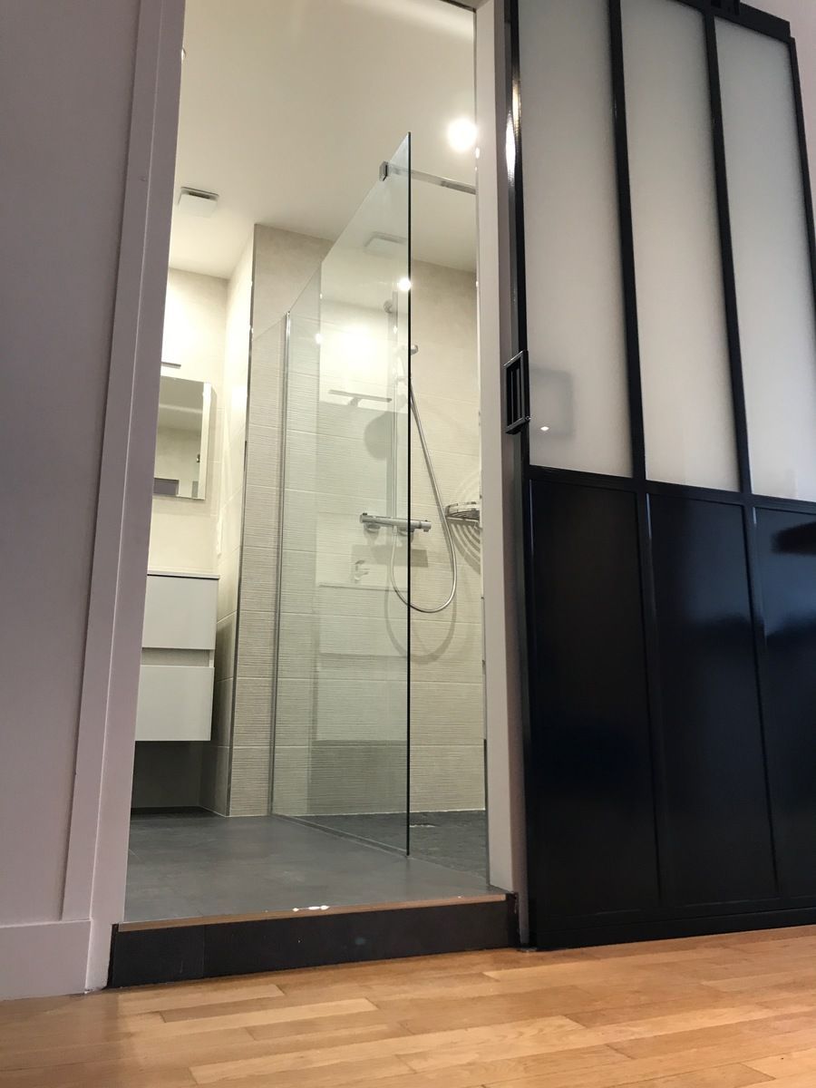 Salle de bains avec douche en verre, meuble-lavabo blanc, porte coulissante à cadre noir.