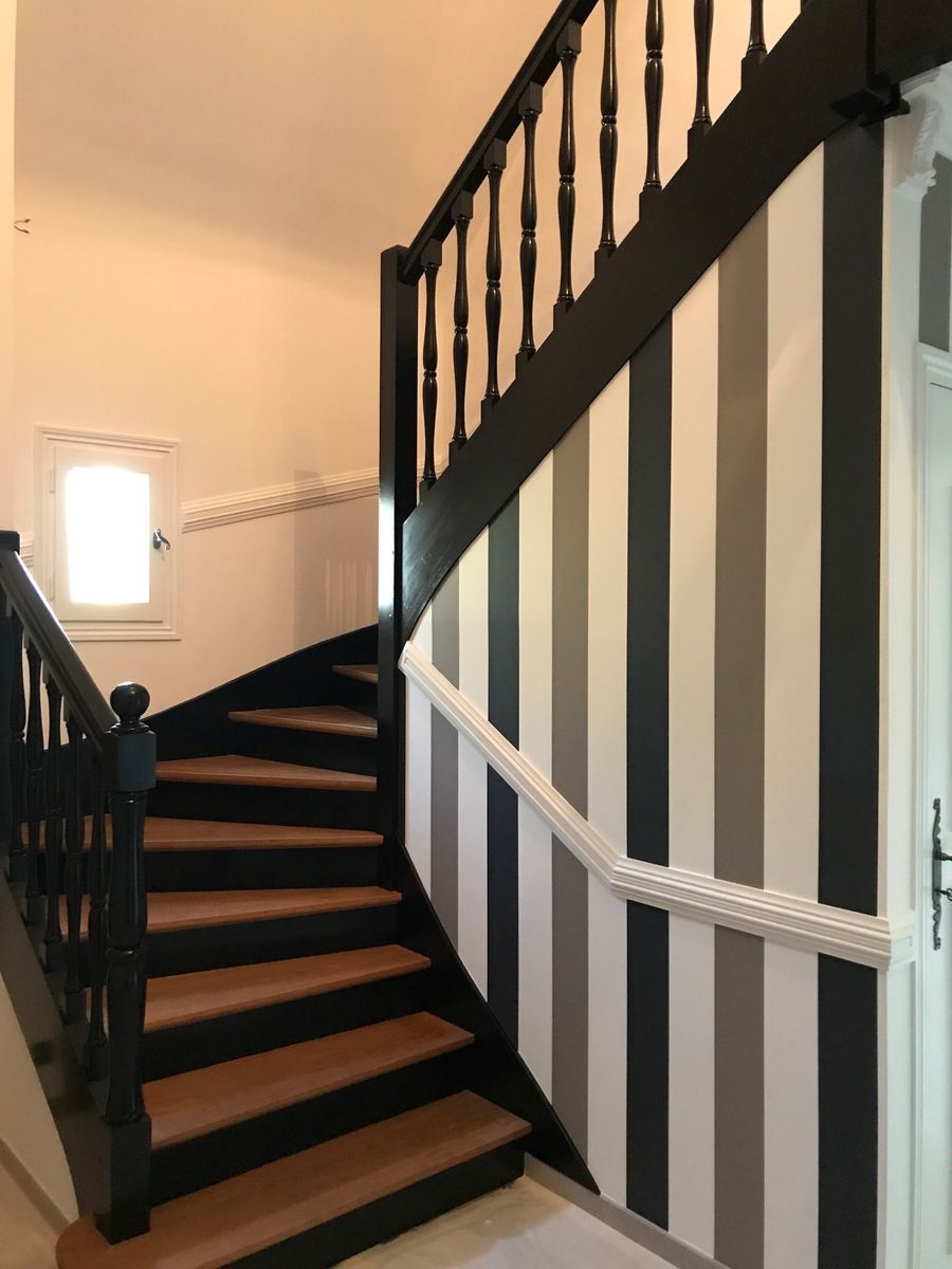 Escalier avec rampes noires et mur rayé gris, blanc et noir.