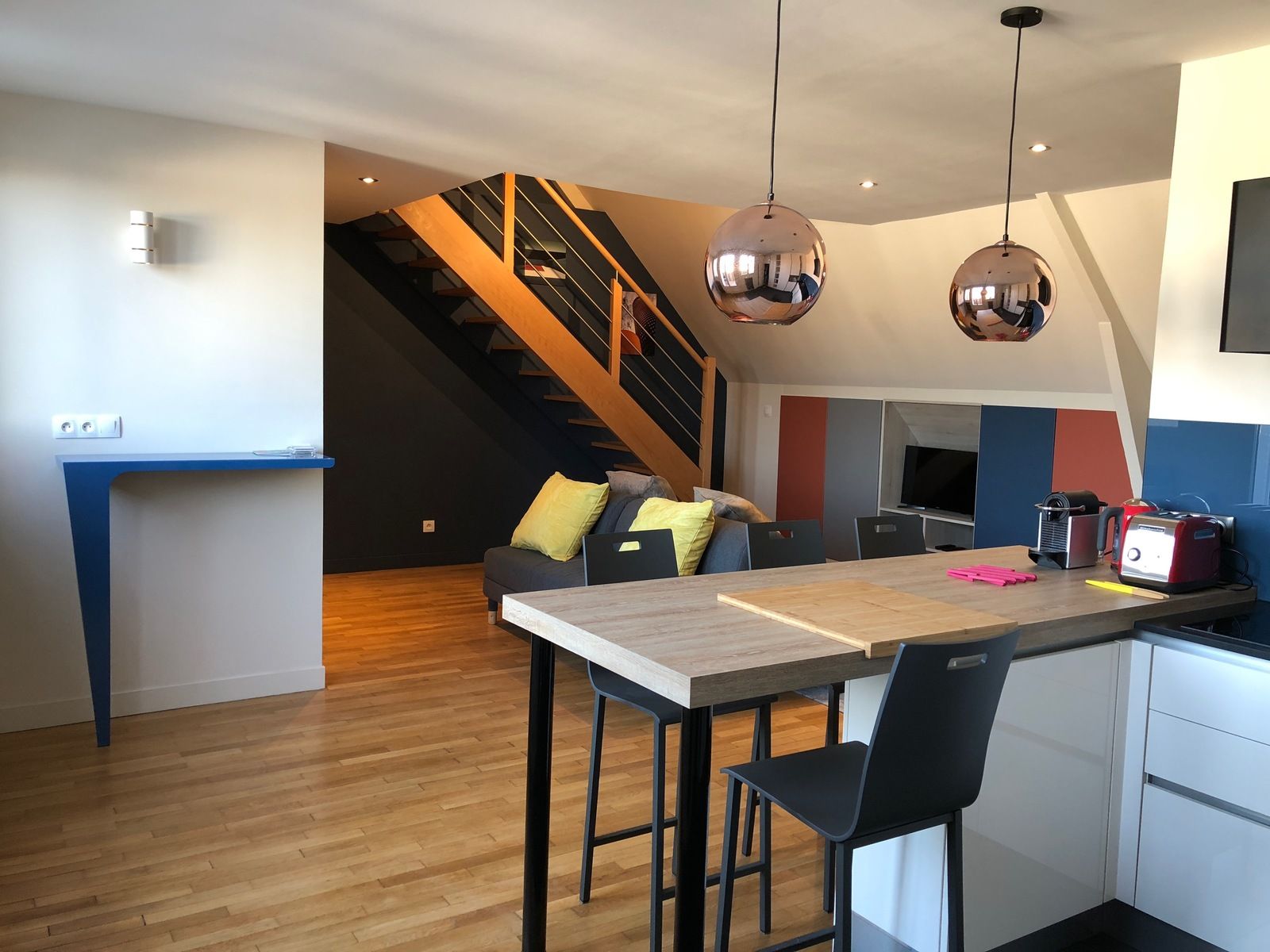 Appartement loft moderne avec cuisine ouverte, bar, escalier et suspensions lumineuses en cuivre.