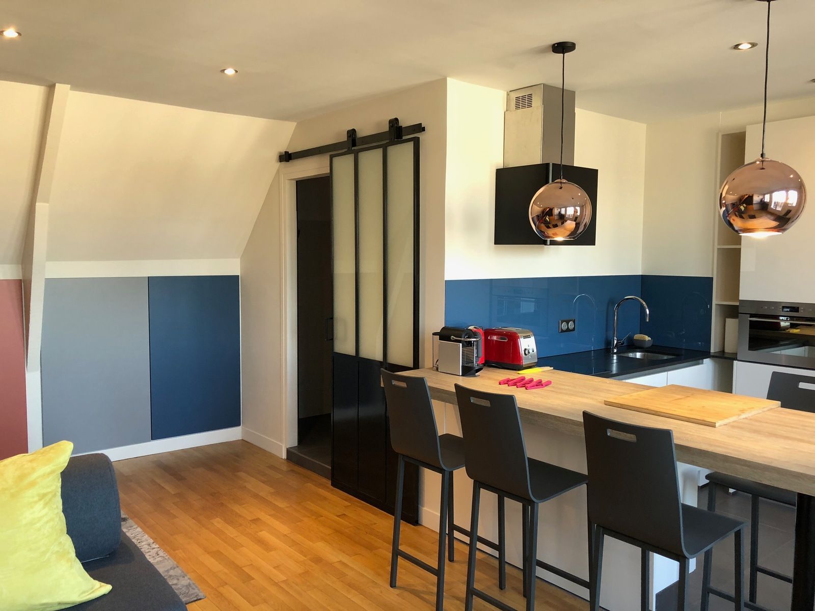 Cuisine moderne avec un bar pour le petit-déjeuner, une crédence bleue et des suspensions lumineuses en cuivre.