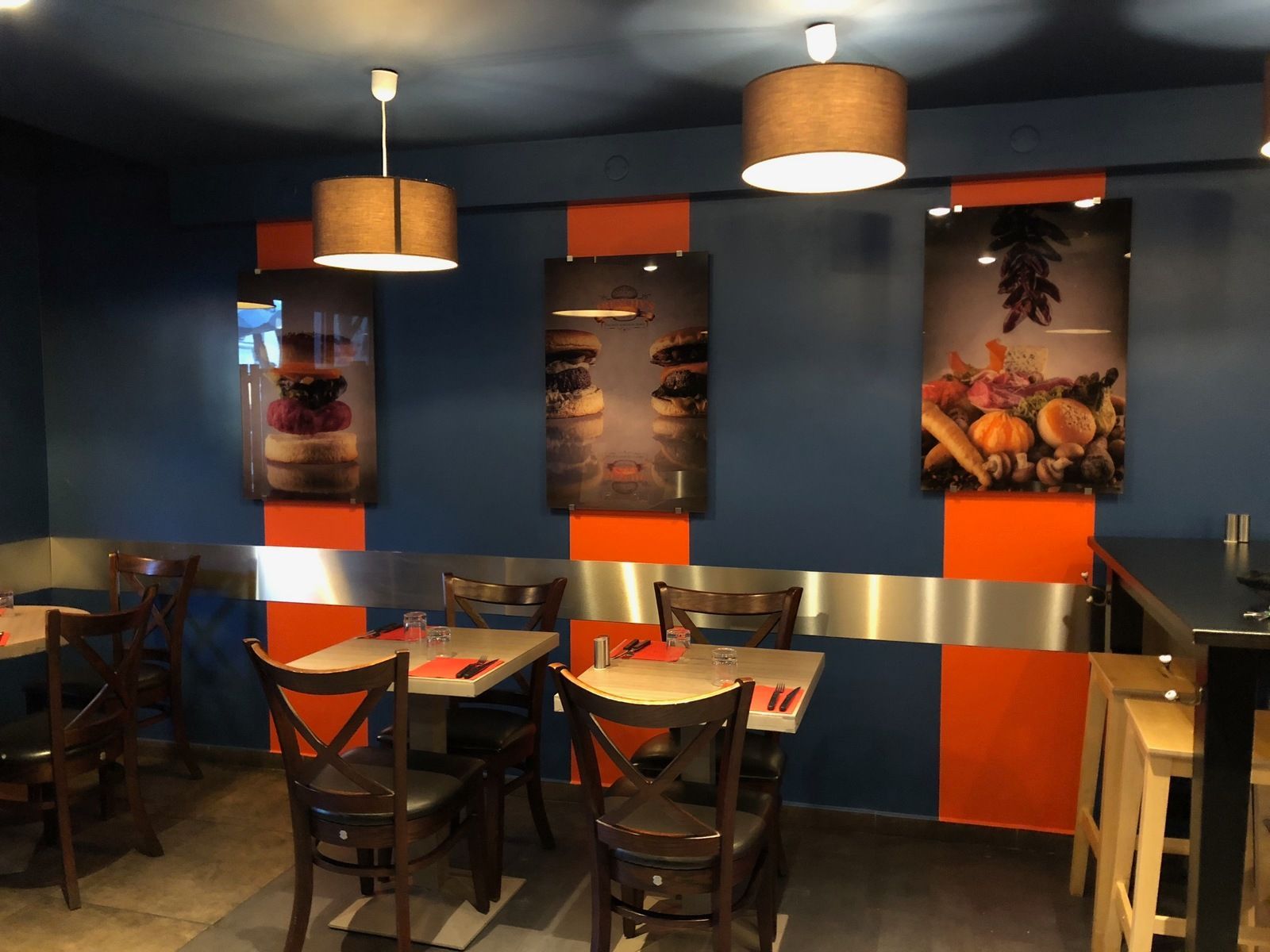 Intérieur de restaurant avec murs bleus, touches d'orange, tables et photos de plats.