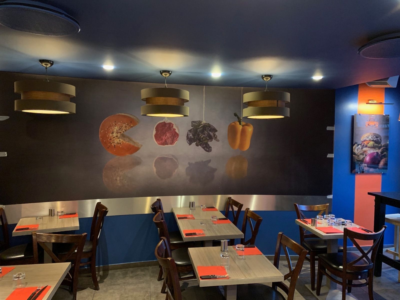 Intérieur de restaurant avec tables, chaises et décorations murales représentant des images de plats sous des guirlandes lumineuses.