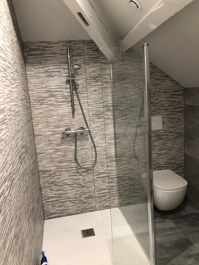 Salle de bains avec douche, toilettes et murs carrelés de carrelage gris texturé. Plafond en pente et porte de douche en verre.