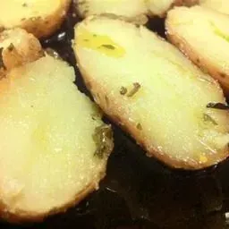 Primer plano de patatas asadas con aceite de oliva y hierbas, en una sartén oscura. Las patatas son de color amarillo claro.