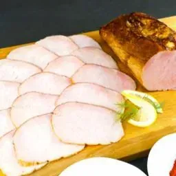 Carne cortada en rodajas, probablemente jamón o pavo, dispuesta sobre una tabla de cortar de madera con una rodaja de limón.