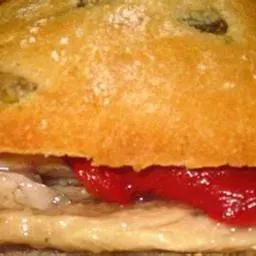 Primer plano de un sándwich con pan dorado, salsa roja y relleno visible.