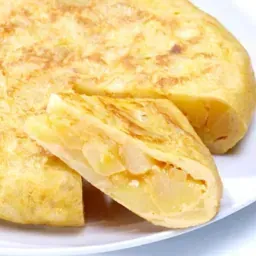 Tortilla española en un plato blanco, cortada para revelar el interior de la patata. La tortilla está dorada y se ven trozos de patata.