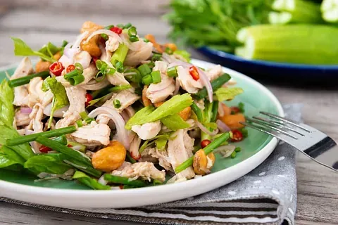 Ensalada de pollo con cebollas verdes, chiles rojos y anacardos en un plato blanco y verde.